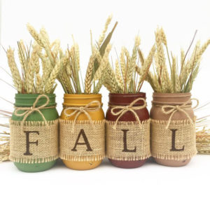 Four mason jars in green, oker, brown and taupe with the letters fall on burlap