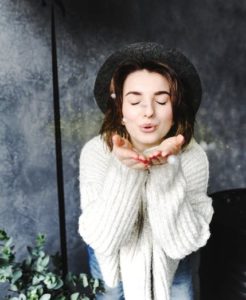 Woman in white sweater wearing a black hat blowing a kiss