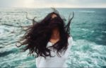 Woman with long black hair waving in the wind by the ocean side