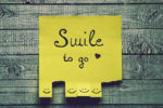 Yellow Post-it with tear off pieces with smileys on them and the text Smile to go