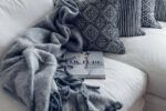 Grey blanket, blue throw pillow and book on an off white couch