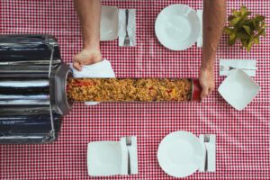 Set table with two hands sliding a family sized meal out of the GoSun Fusion solar cooker