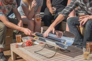 Group of people around the GoSun Sport solar oven while one man touches the tube to show it doesn't get hot