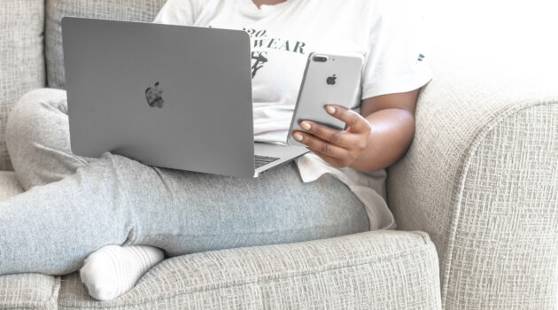 Woman of color in loungewear on couch with laptop and smartphone