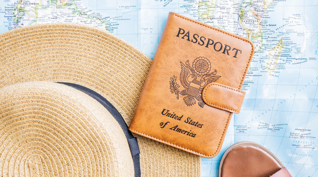 A sun hat, brown sandals, and a brown leather passport holder placed on a world map