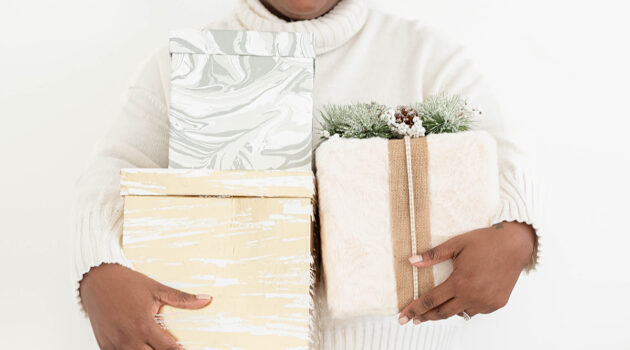 Close up of the arms of a woman in a white nordic sweater holding a pack of neutral toned presents