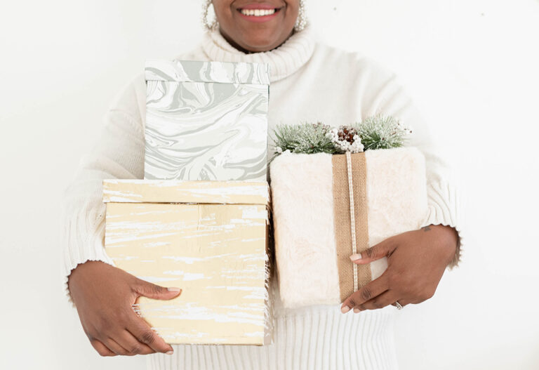 Close up of the arms of a woman in a white nordic sweater holding a pack of neutral toned presents